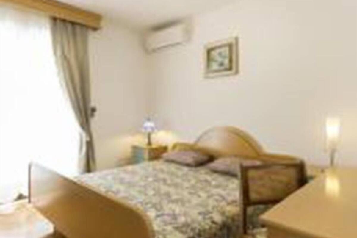 A bedroom with a bed, bedside table, lamp, and a small picture on the wall.