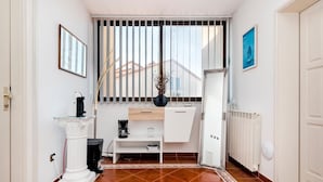Ein Hotelzimmer mit weißem Schreibtisch, einer Kaffeemaschine, einer Vase und einer Heizung.