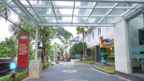 Entrada de hotel con una cubierta de vidrio, un letrero que enumera servicios como habitaciones de hotel, salas de reuniones y un spa con masajes, además de una estatua de una criatura mítica.