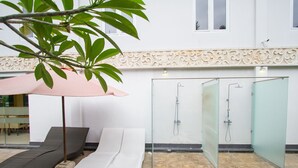 Un área de spa con ducha envuelta en cristal, una silla de descanso y una pequeña mesa bajo un paraguas rosa.