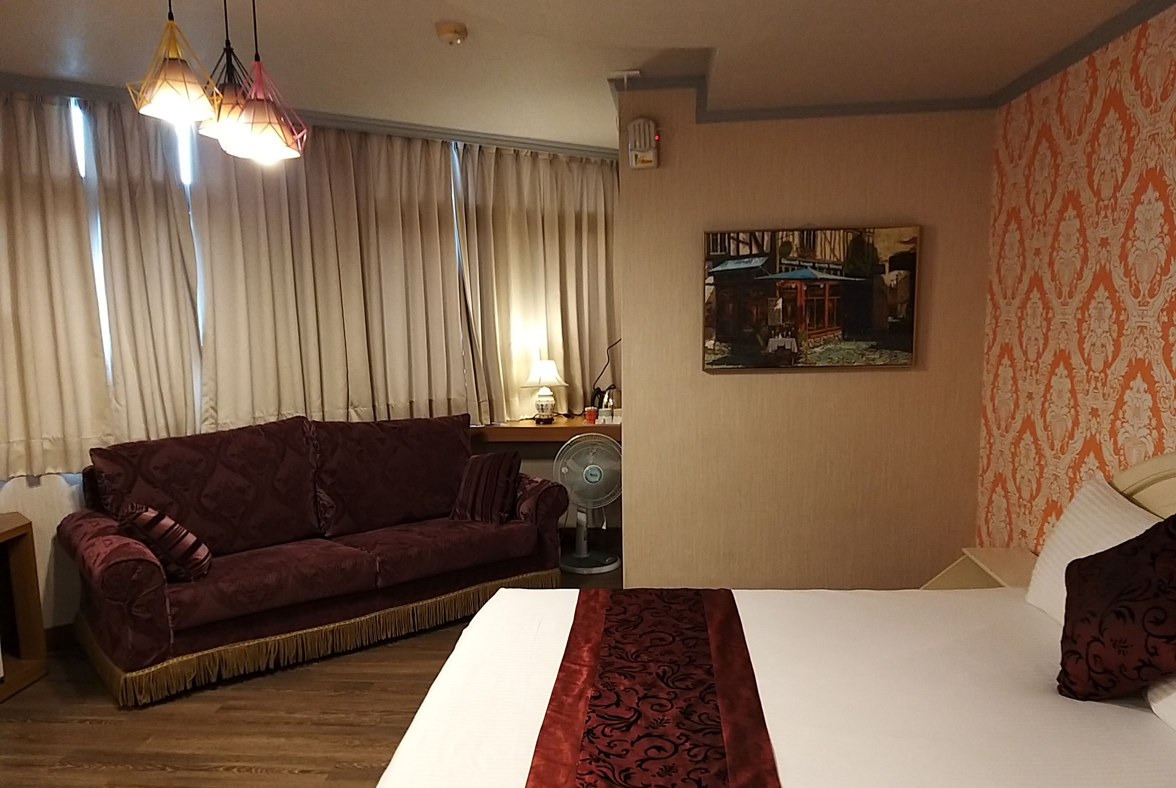 A hotel room with a large bed, a red sofa, a desk with a lamp, and a painting on the wall.