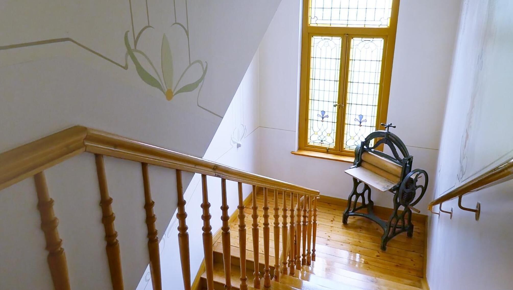 A wooden staircase with a handrail, a window with a yellow frame, and a vintage sewing machine on the landing.