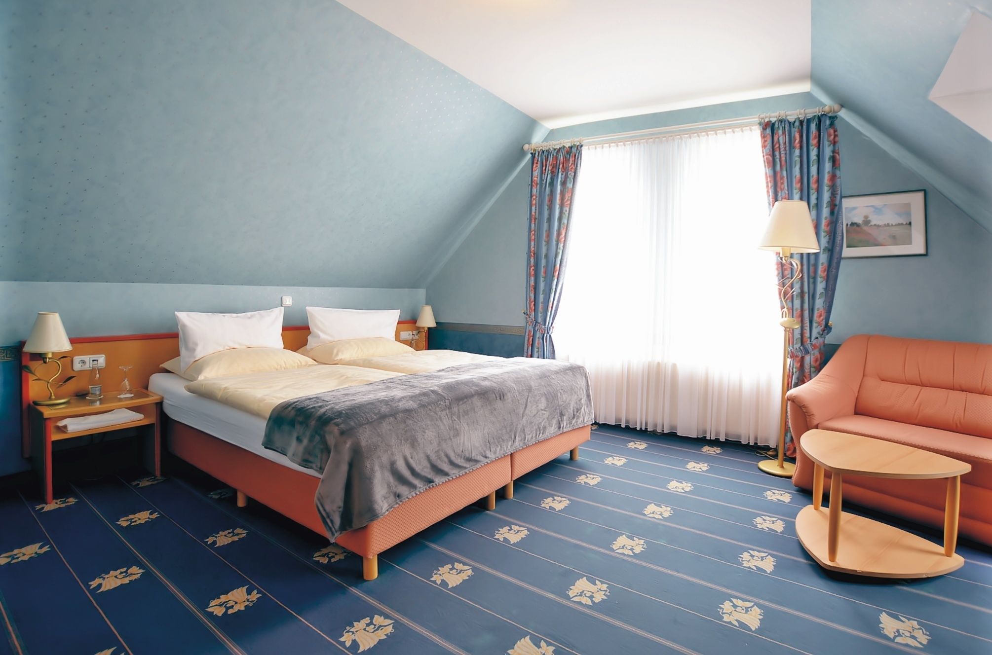 A hotel room with a large bed, a chair, a small table, and a window with curtains.