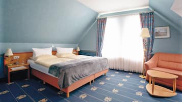 A hotel room with a large bed, a chair, a small table, and a window with curtains.