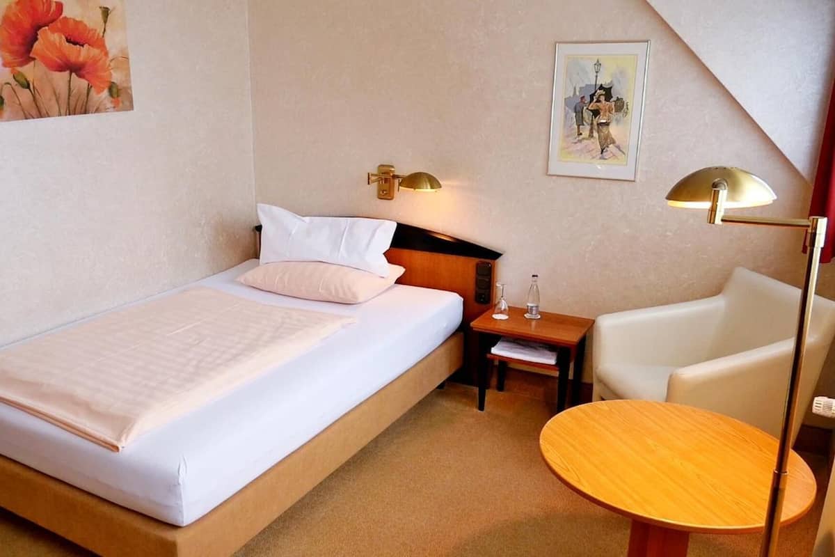 Ett hotellrum med en säng, ett nattduksbord, en lampa, en stol och ett runt bord.