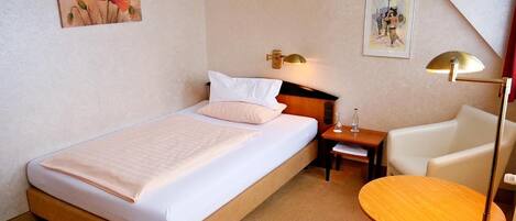 A hotel room with a bed, bedside table, lamp, chair, and a round table.