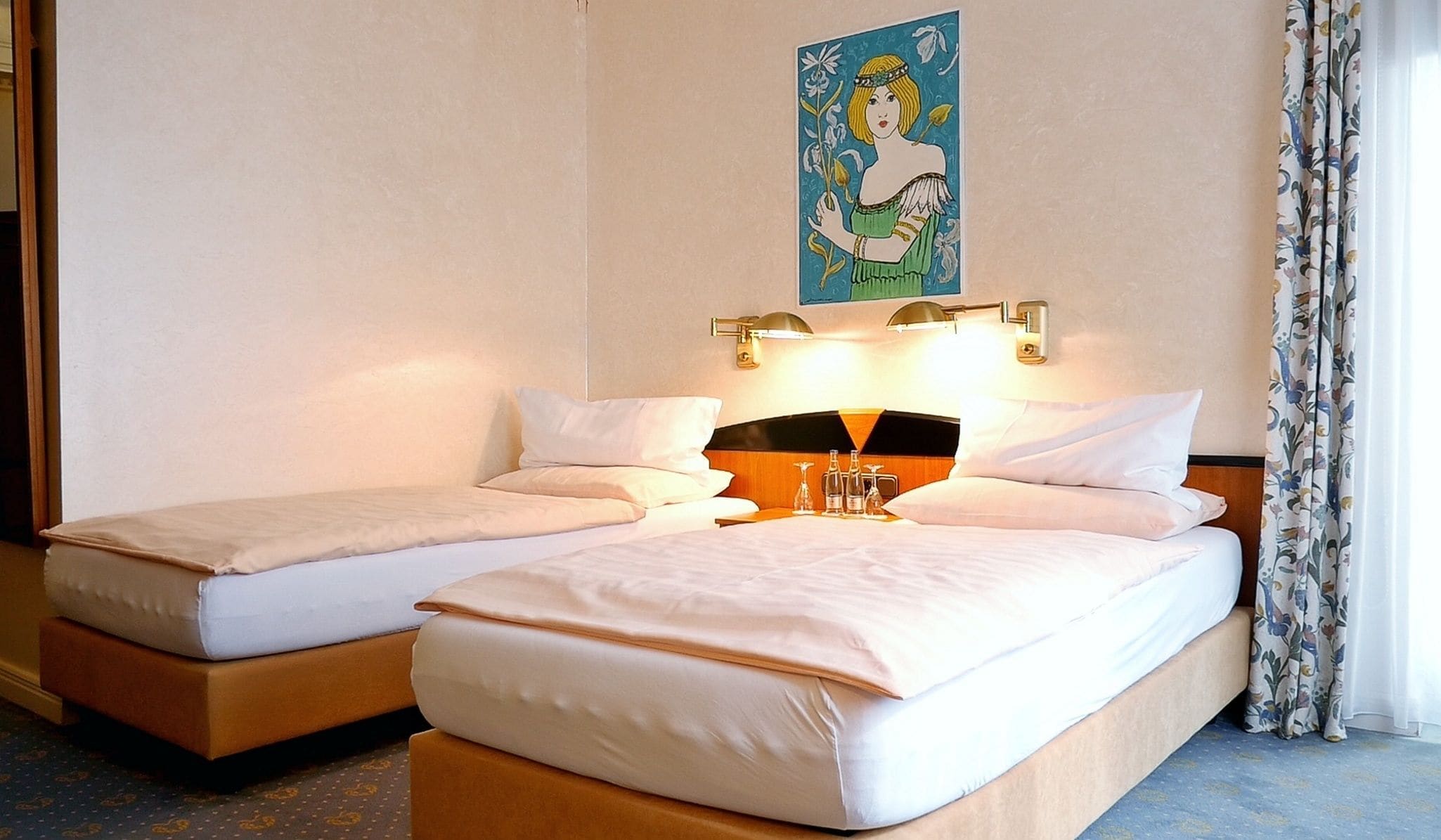 A hotel room with two single beds, a nightstand with a lamp, and a painting on the wall.