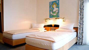 A hotel room with two single beds, a nightstand with a lamp, and a painting on the wall.