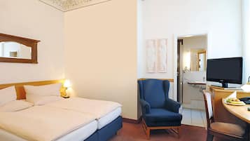 A hotel room with a bed, a chair, a desk with a computer, and a television.