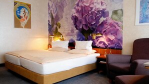 Una habitación de hotel con una cama, una mesita de noche, una silla y un mural floral grande.
