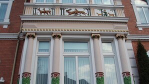 Un edificio con amplios ventanales, columnas decorativas y un balcón con esculturas de animales.
