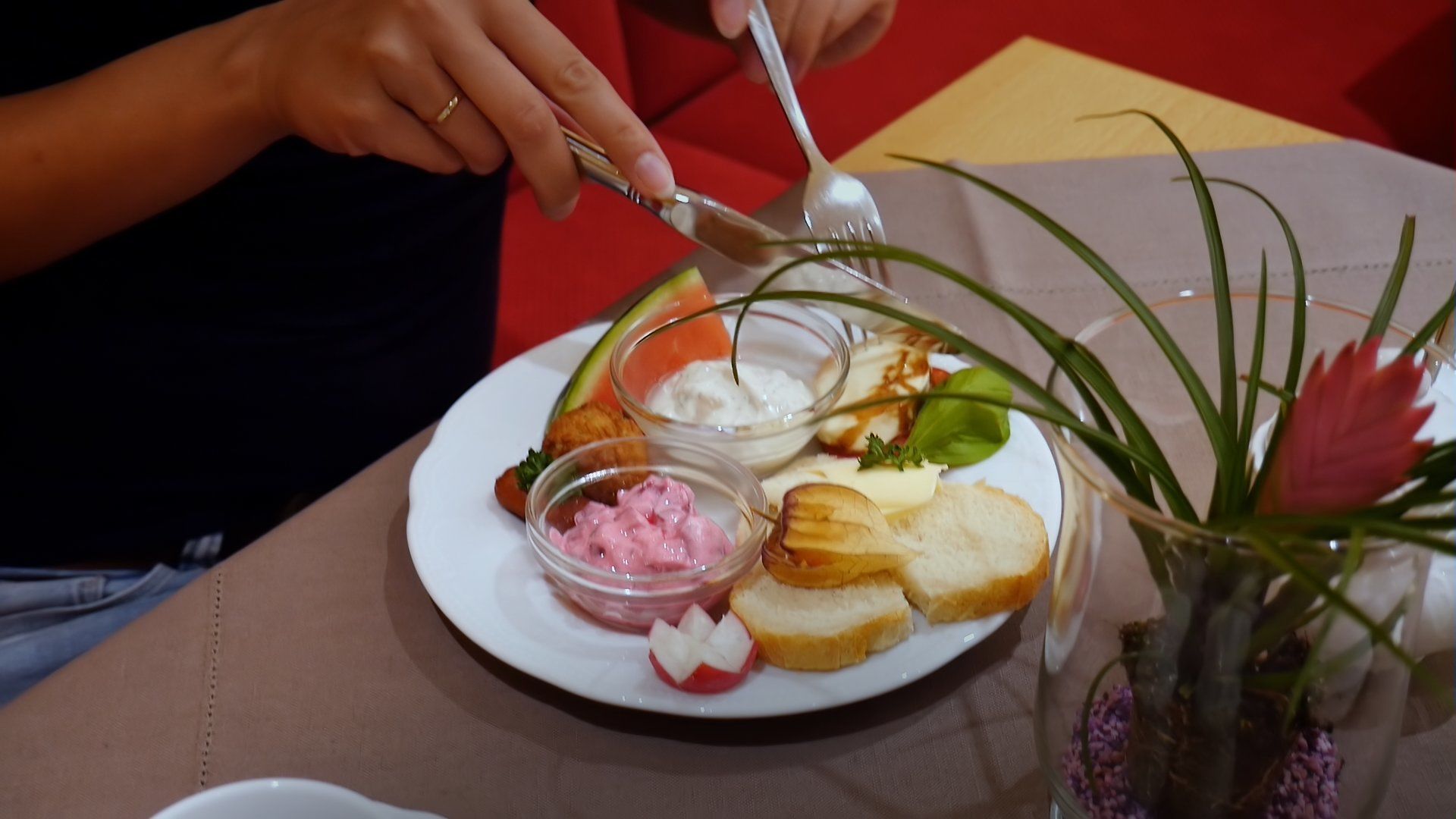 A person serving food from a plate with various items including bread, a small bowl of pink substance, and a small bowl of white substance.