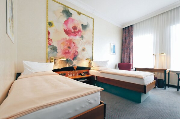 Habitación de hotel con dos camas, una obra de arte floral grande en la pared, un escritorio con lámpara y una silla.