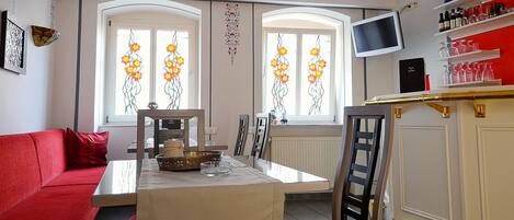 A dining area with a table set for two, a red sofa, and a TV mounted on the wall.