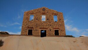 Un edificio de piedra con tres ventanas y una puerta, sobre un cielo azul despejado.