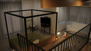 Una sala de estar moderna con piso de madera, un sofá blanco, un televisor sobre un mueble bajo y una mesa de comedor con sillas.