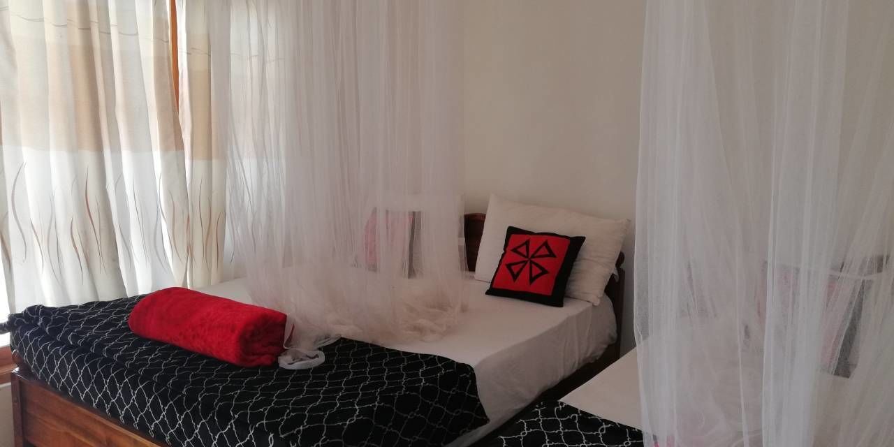 A bed with a black and white patterned bedspread, a red pillow, and a white pillow with a geometric design.