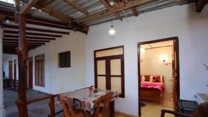 Un espace repas comprenant une table et des chaises, un plafond en bois et une porte-fenêtre donnant sur une chambre.