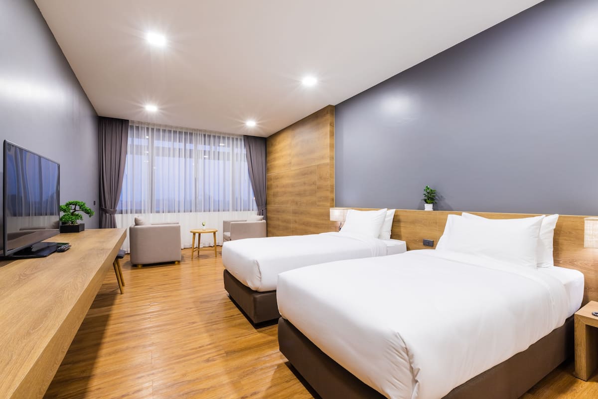 Een moderne hotelkamer met twee bedden, een houten bureau, een televisie, een klein tafeltje en een raam met gordijnen.