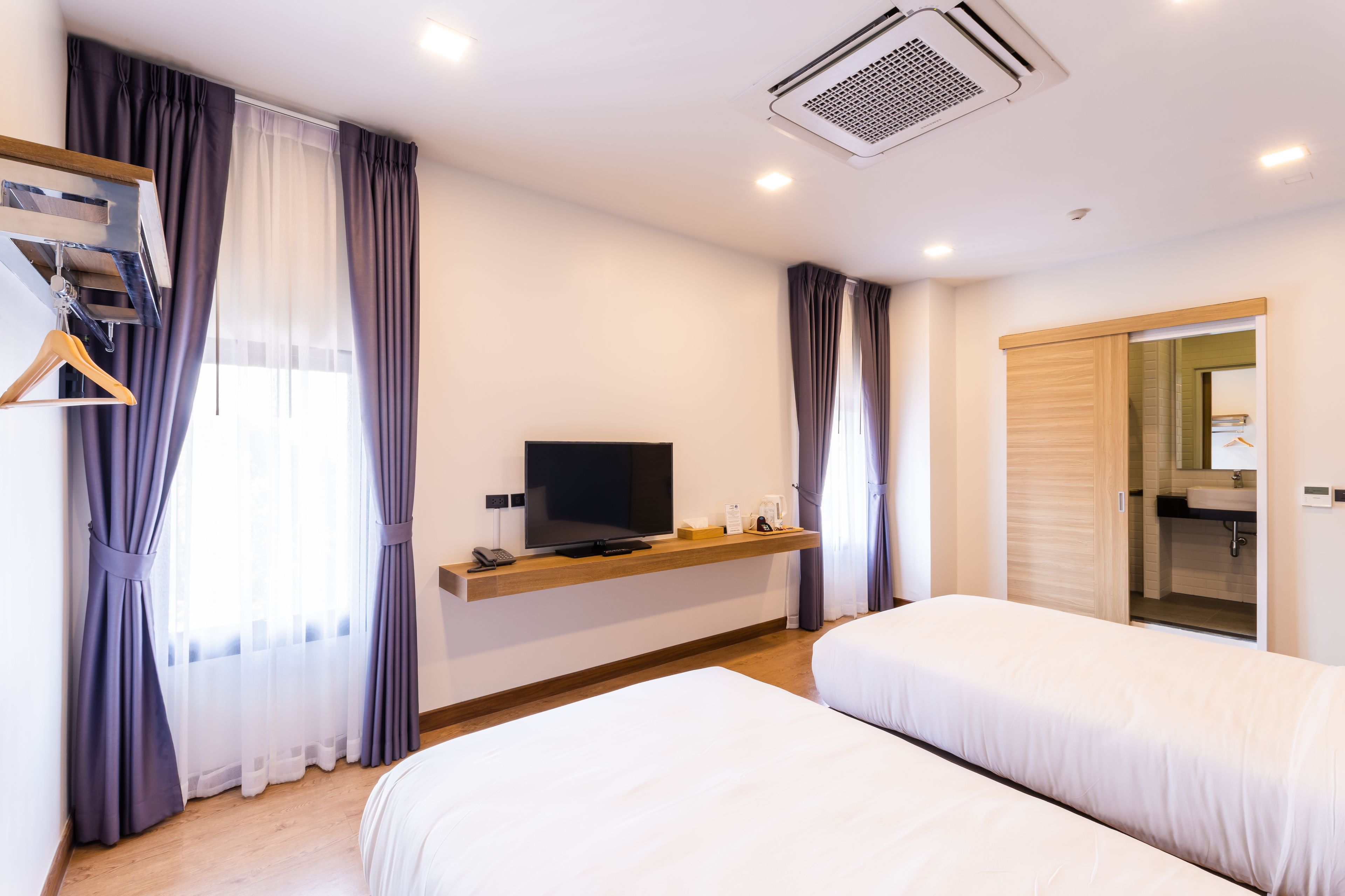 Une chambre d’hôtel avec deux lits, un téléviseur posé sur une étagère en bois, une armoire et une salle de bain visible à travers une porte ouverte.