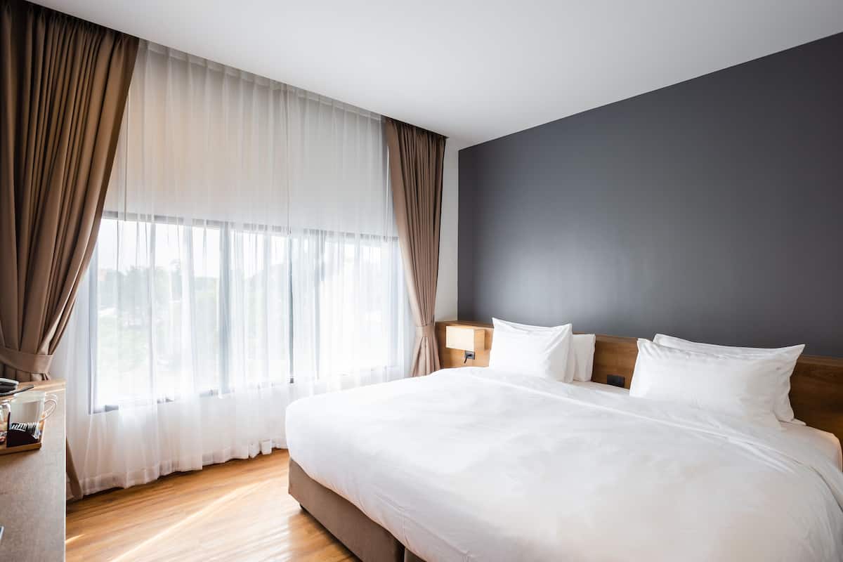 Een net opgemaakt bed met witte lakens, een houten hoofdbord en een nachtkastje met een lamp.
