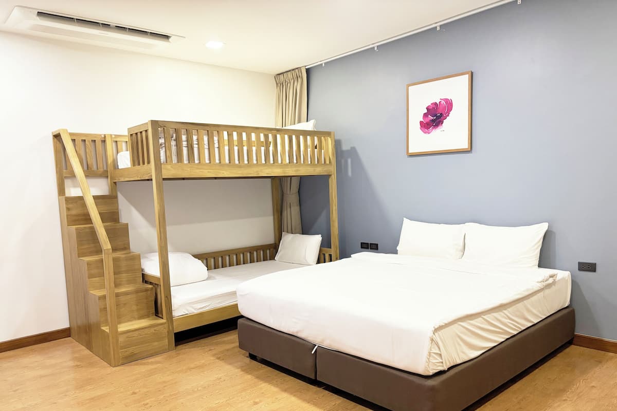Een kamer met een stapelbed, een onderbed, houten vloeren, een wandairconditioner en een ingelijst kunstwerk.