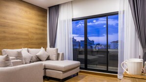 Una sala moderna con sofá, un ventanal con cortinas y vista a edificios.