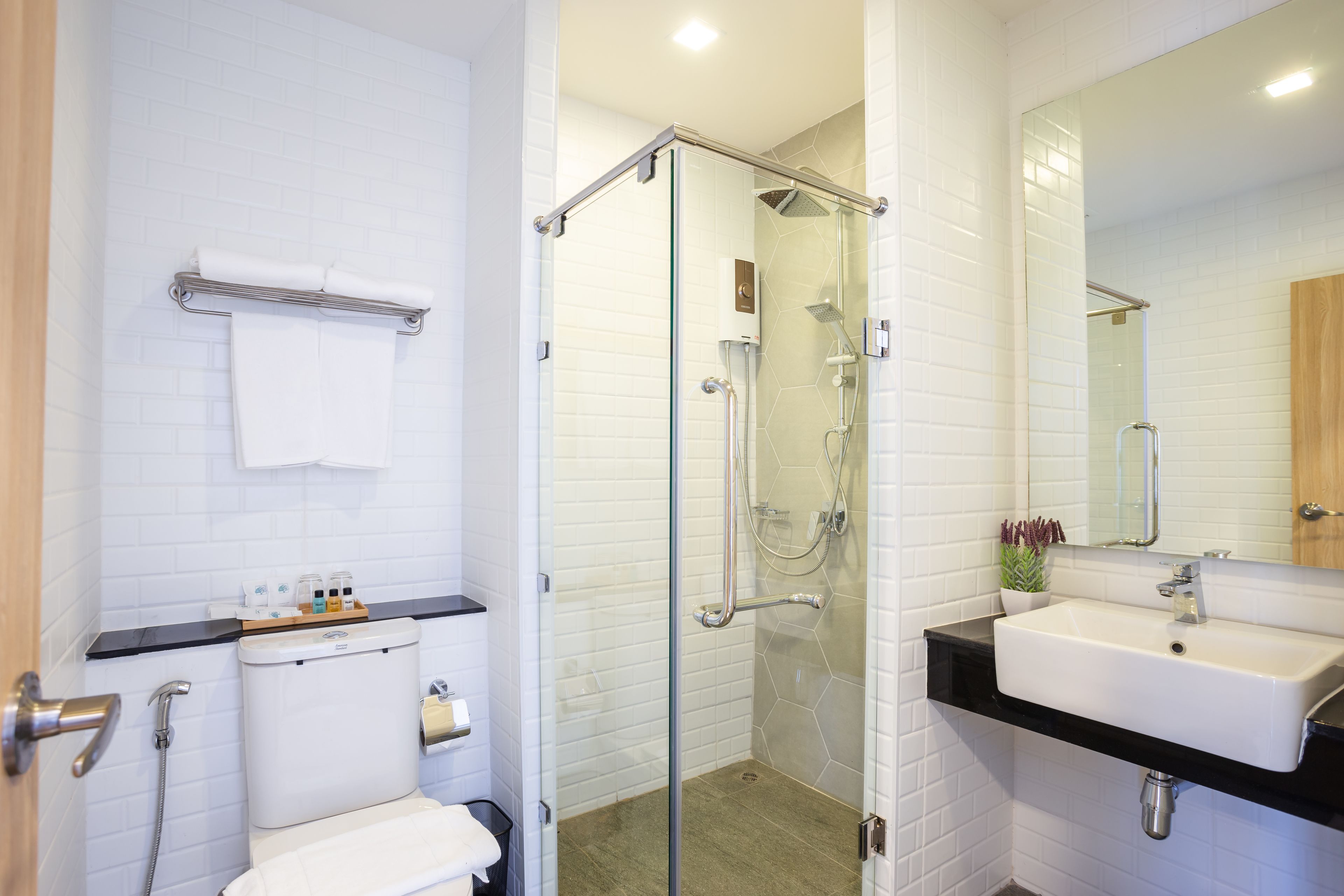 Un bagno moderno con doccia a parete in vetro, un water bianco, un piano lavabo nero e uno specchio grande sopra il lavandino.