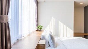 Una habitación de hotel moderna con una cama, una planta pequeña en maceta y vistas al exterior a través de cortinas traslúcidas.