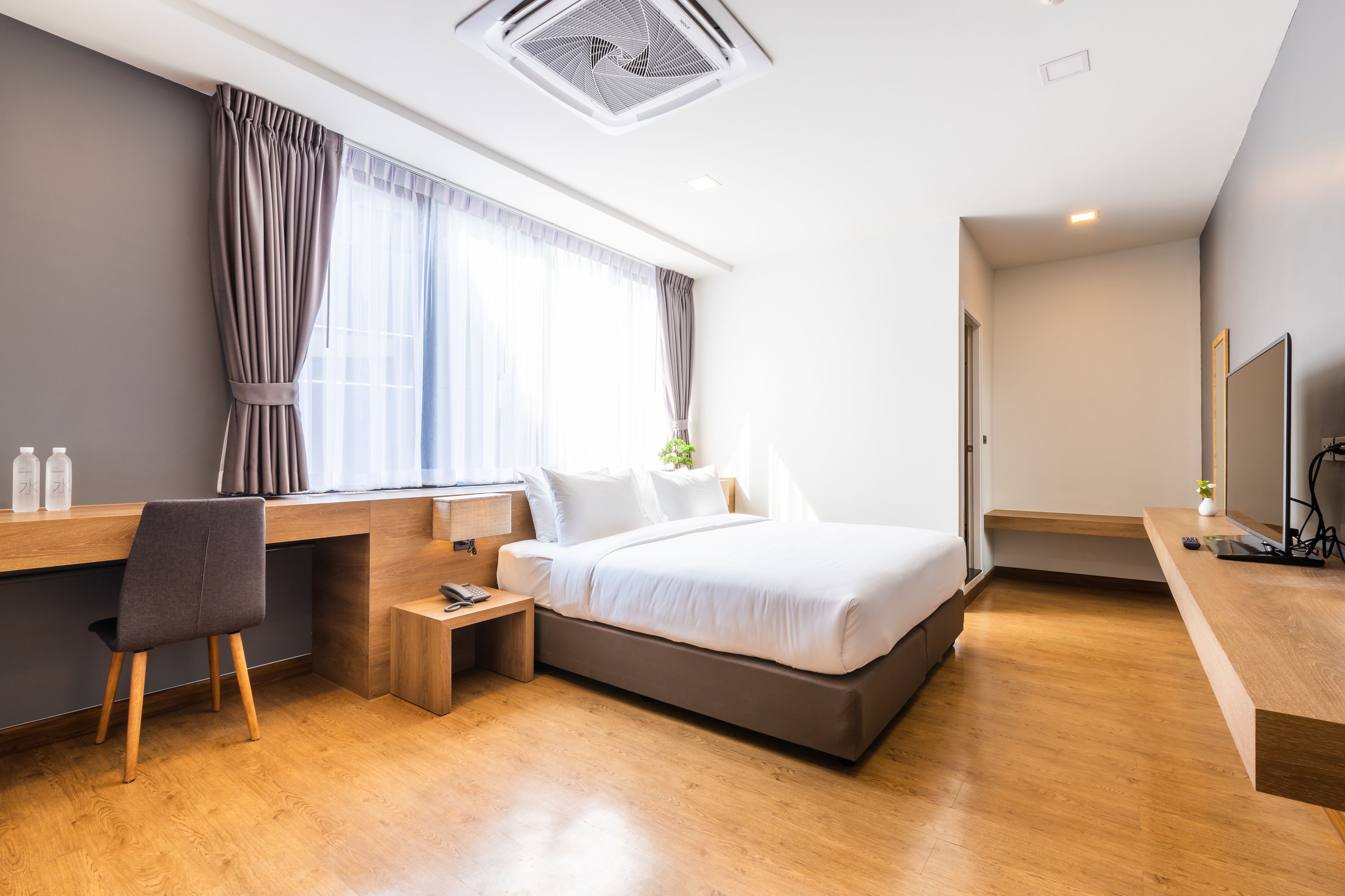A modern hotel room with a bed, desk, chair, and a small bedside table.