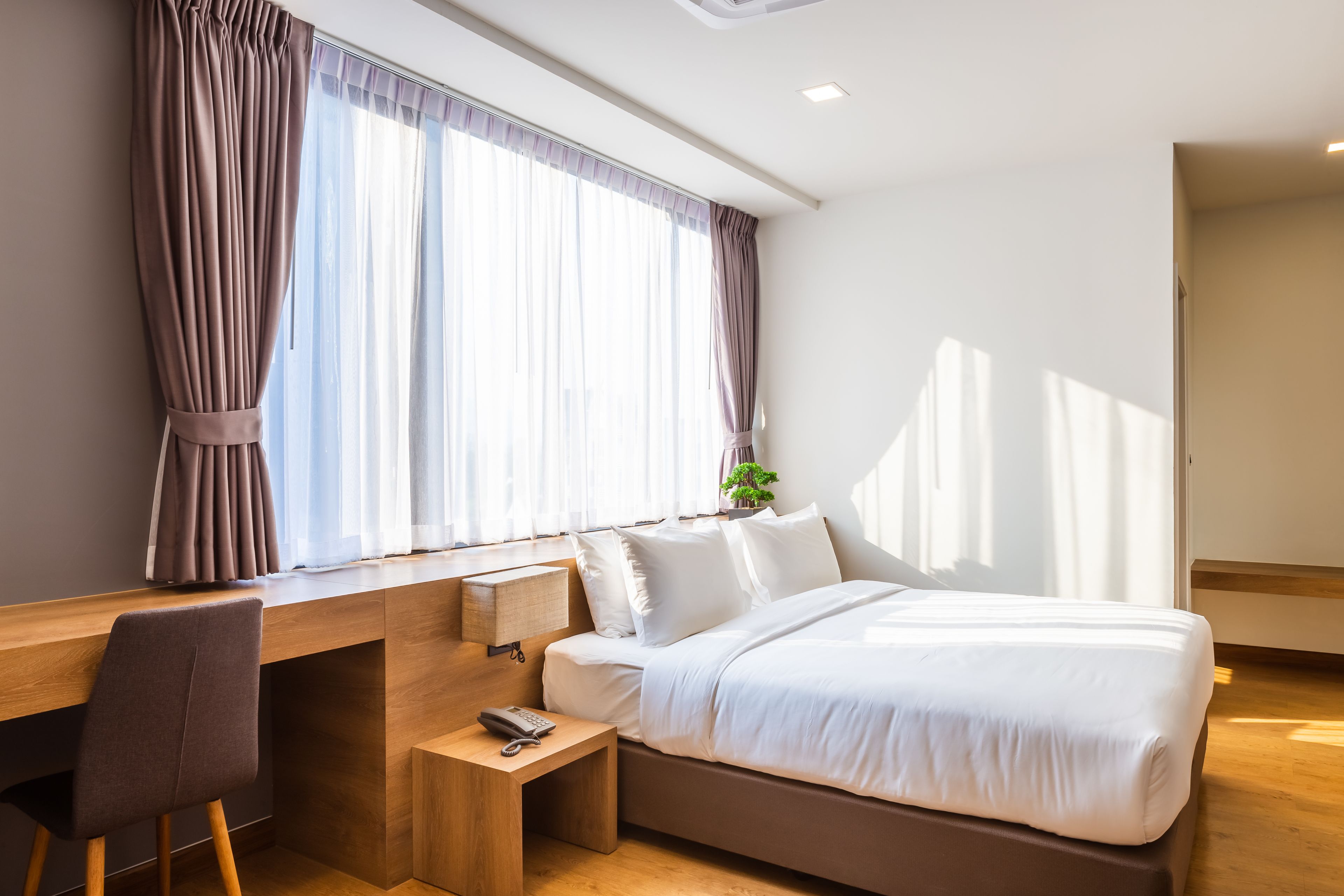 Ett modernt hotellrum med ett skrivbord i trä, en bekväm säng och ett stort fönster med gardiner.