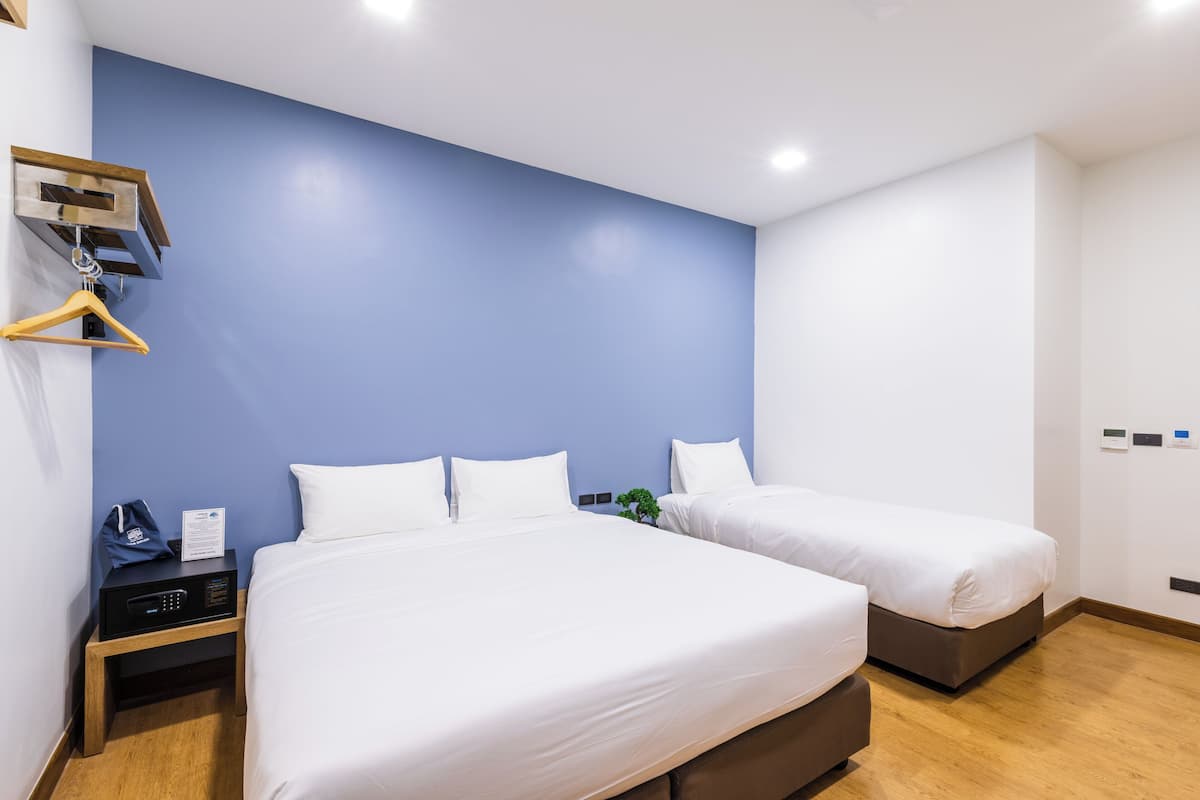Een hotelkamer met twee bedden, een houten nachtkastje, een blauwe accentmuur en een kleine plant.