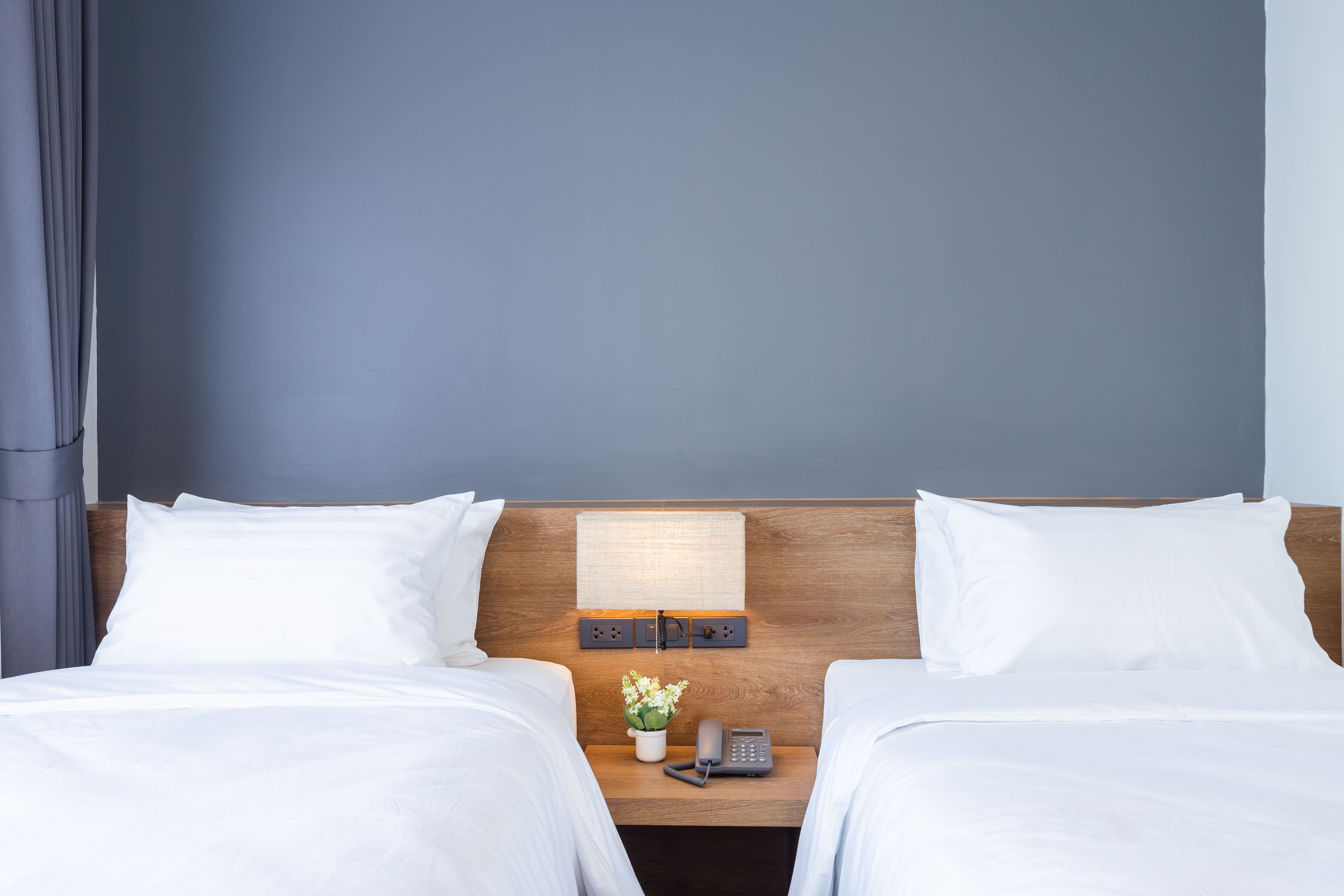A hotel room with two beds, a nightstand with a lamp, a phone, and a small flower arrangement.