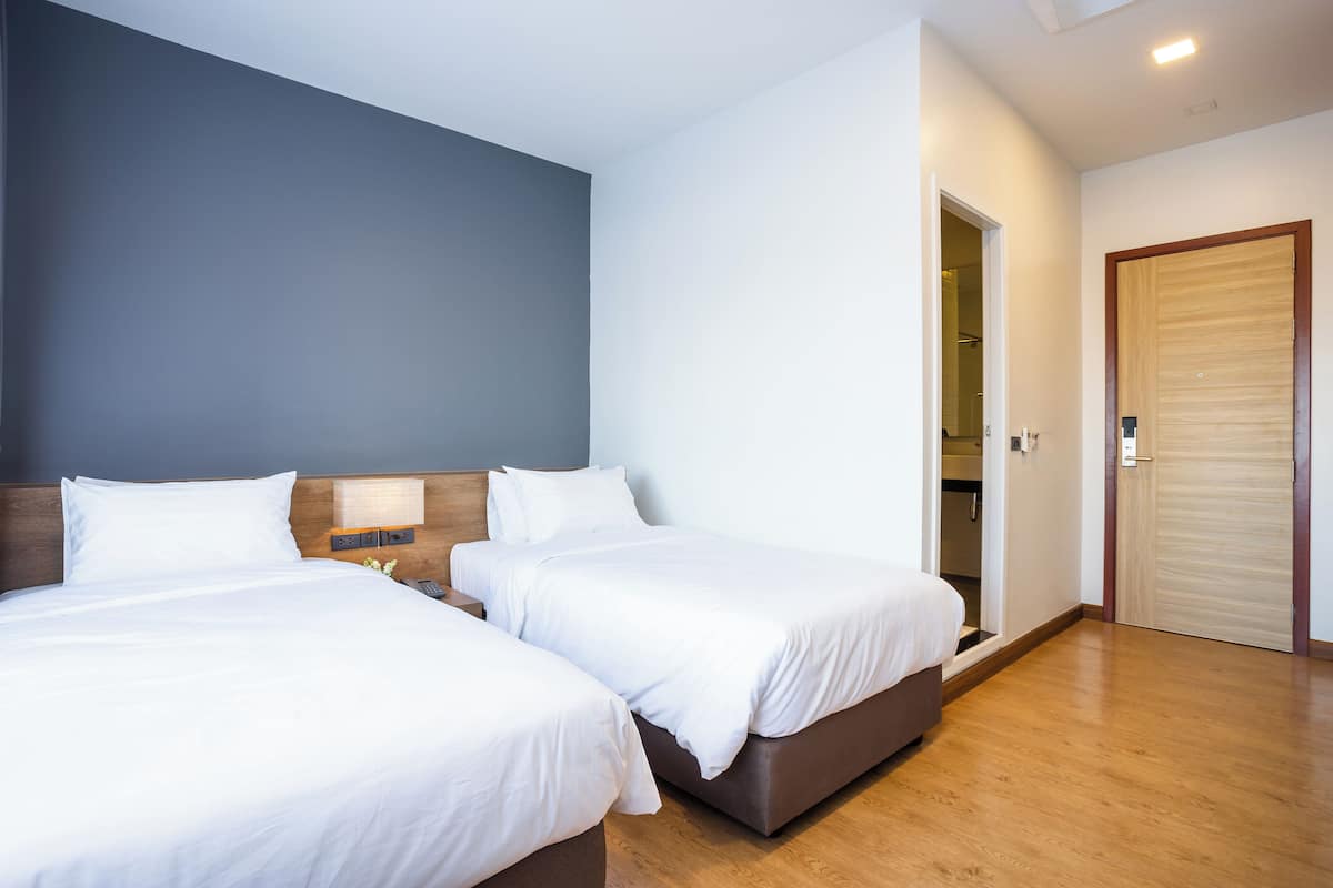 Een hotelkamer met twee bedden, houten vloeren, een blauwe accentmuur en een houten deur.