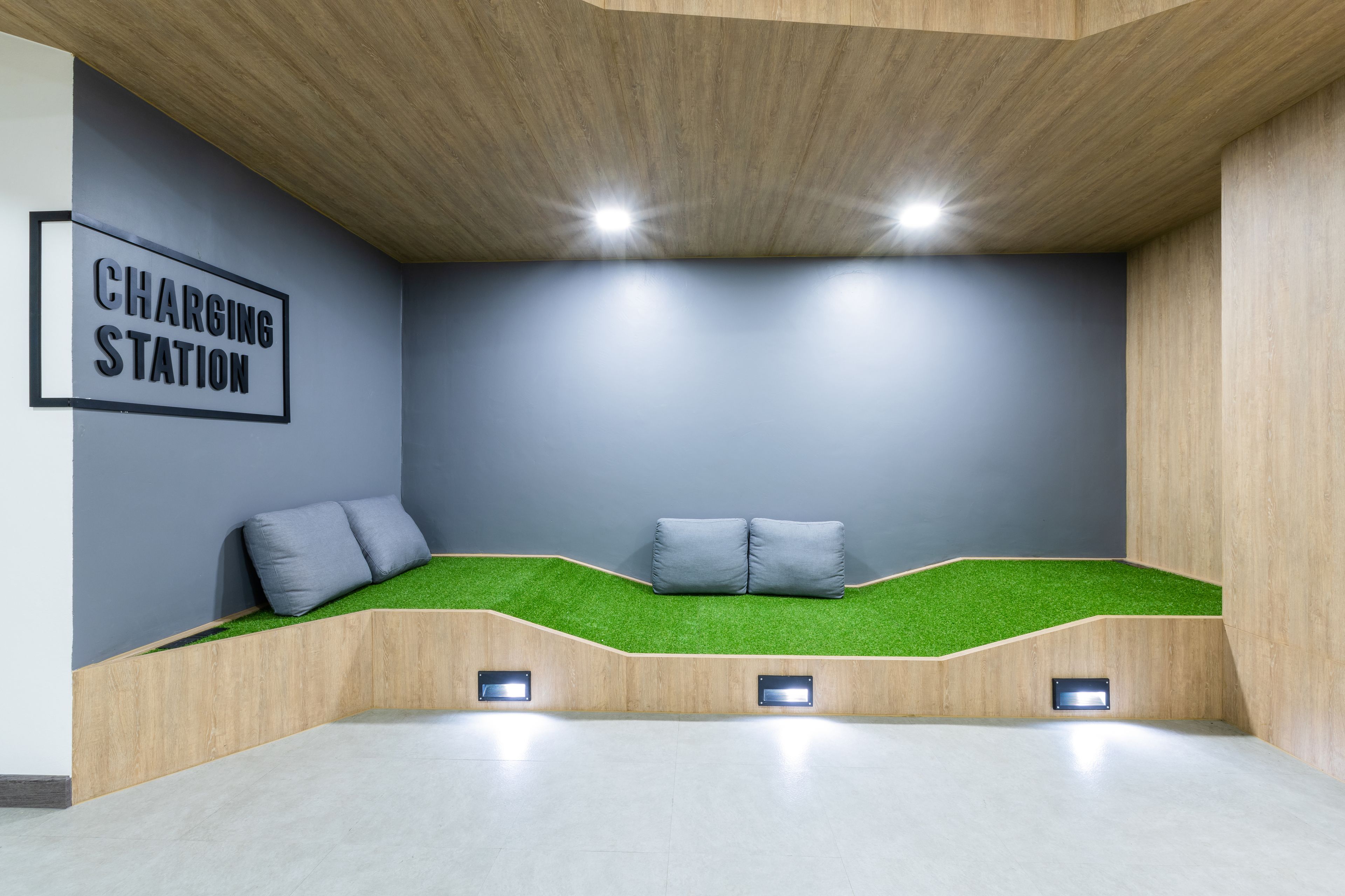 A modern room with a charging station sign, a seating area with green artificial grass, and recessed lighting.
