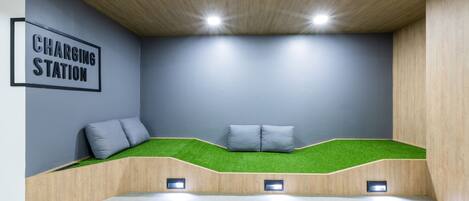A modern room with a charging station sign, a seating area with green artificial grass, and recessed lighting.