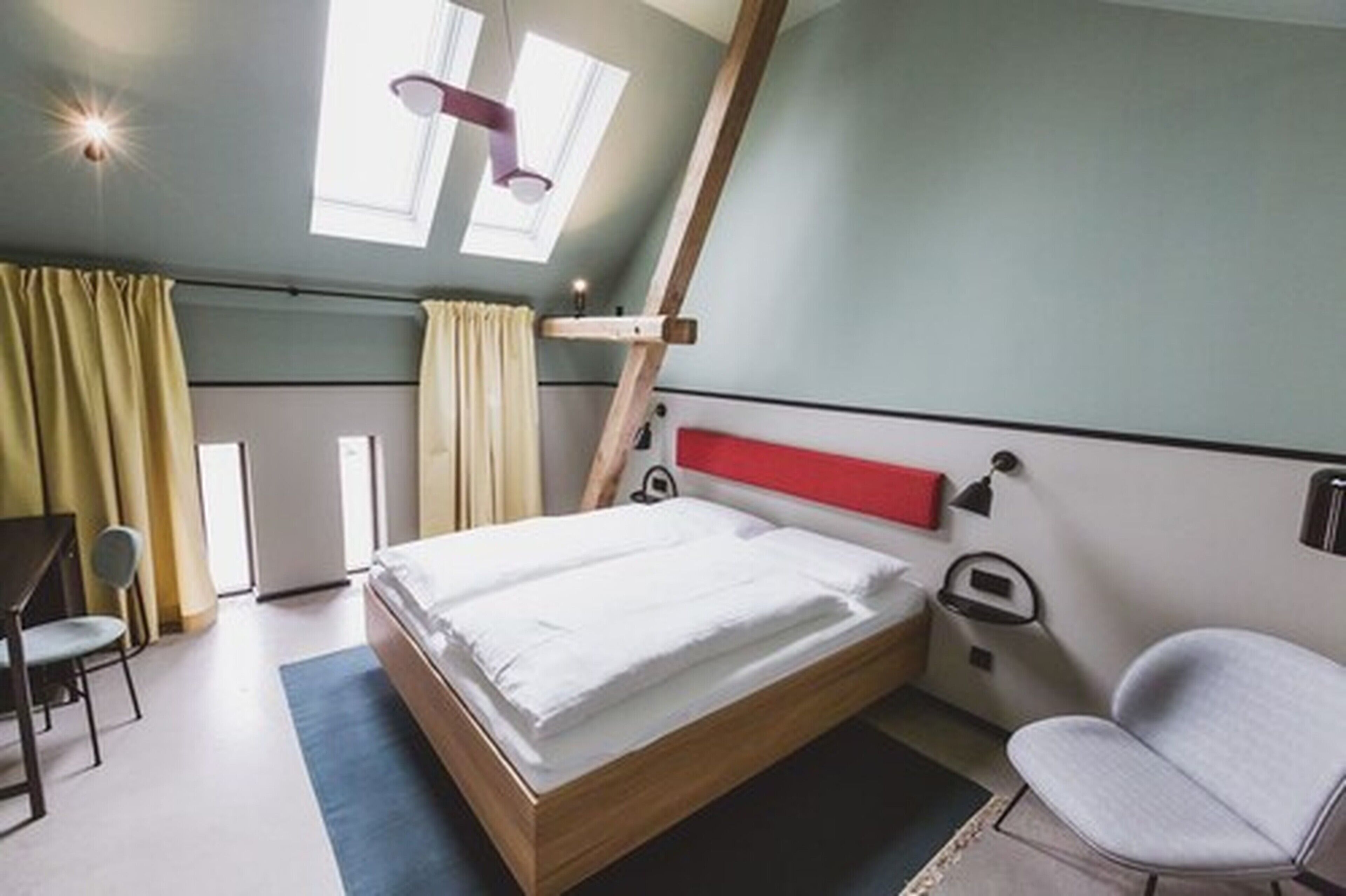 A modern hotel room with a bed, a desk, a chair, and a window with curtains.