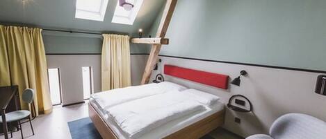A modern hotel room with a bed, a desk, a chair, and a window with curtains.