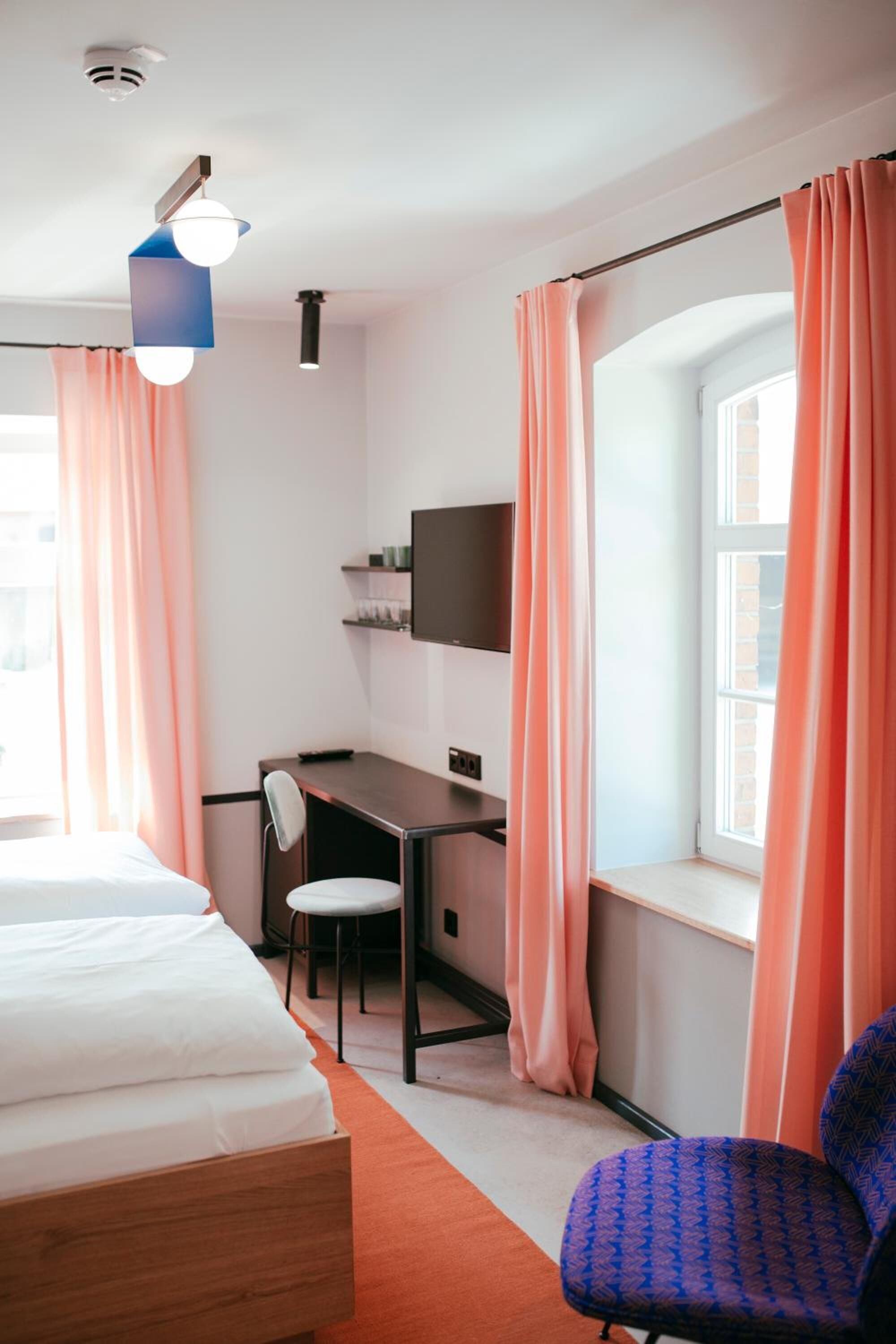 A hotel room with a bed, desk, chair, and a TV on the wall.