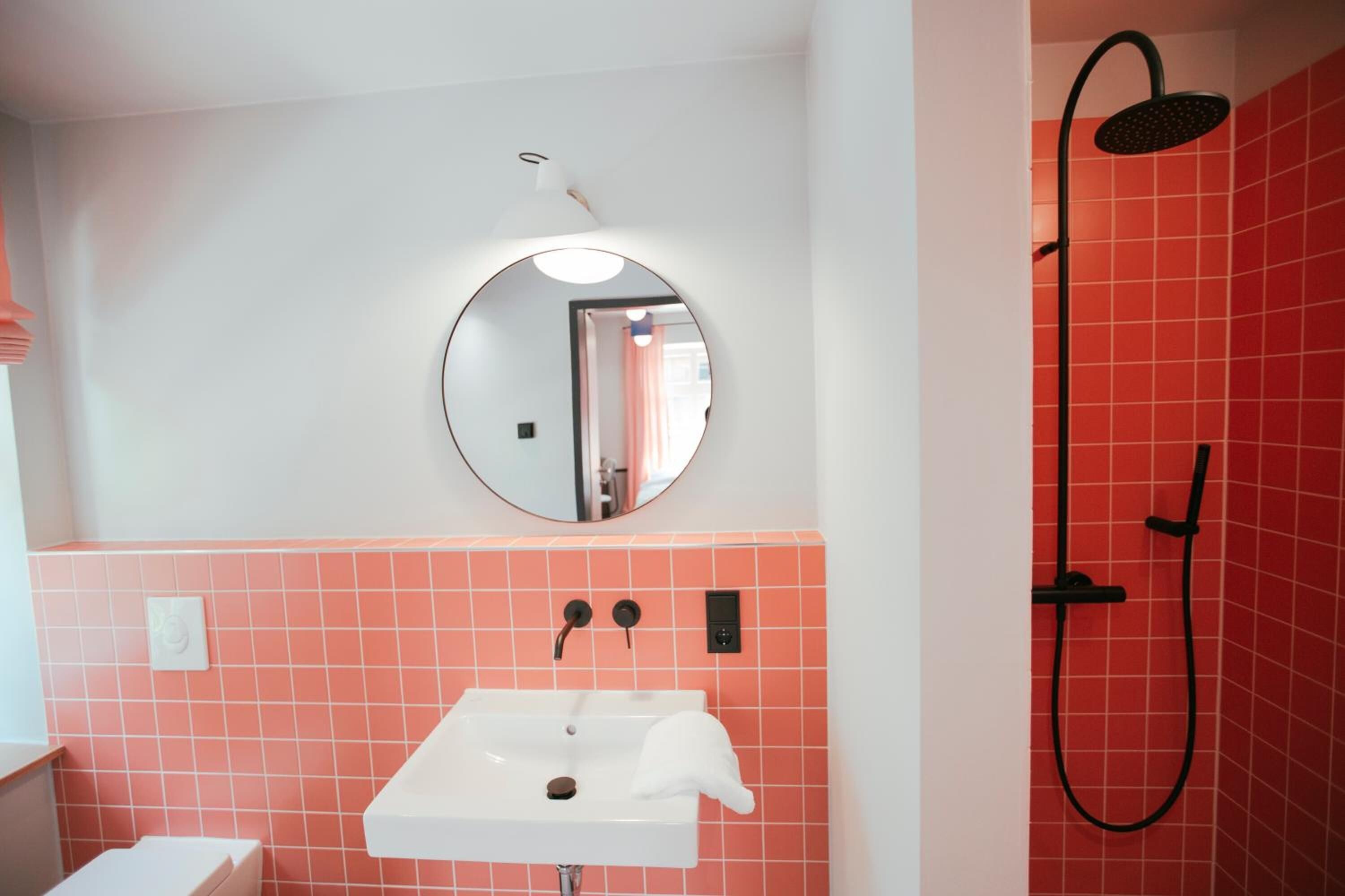 A bathroom with a white sink, a round mirror, and a shower with a black hose.