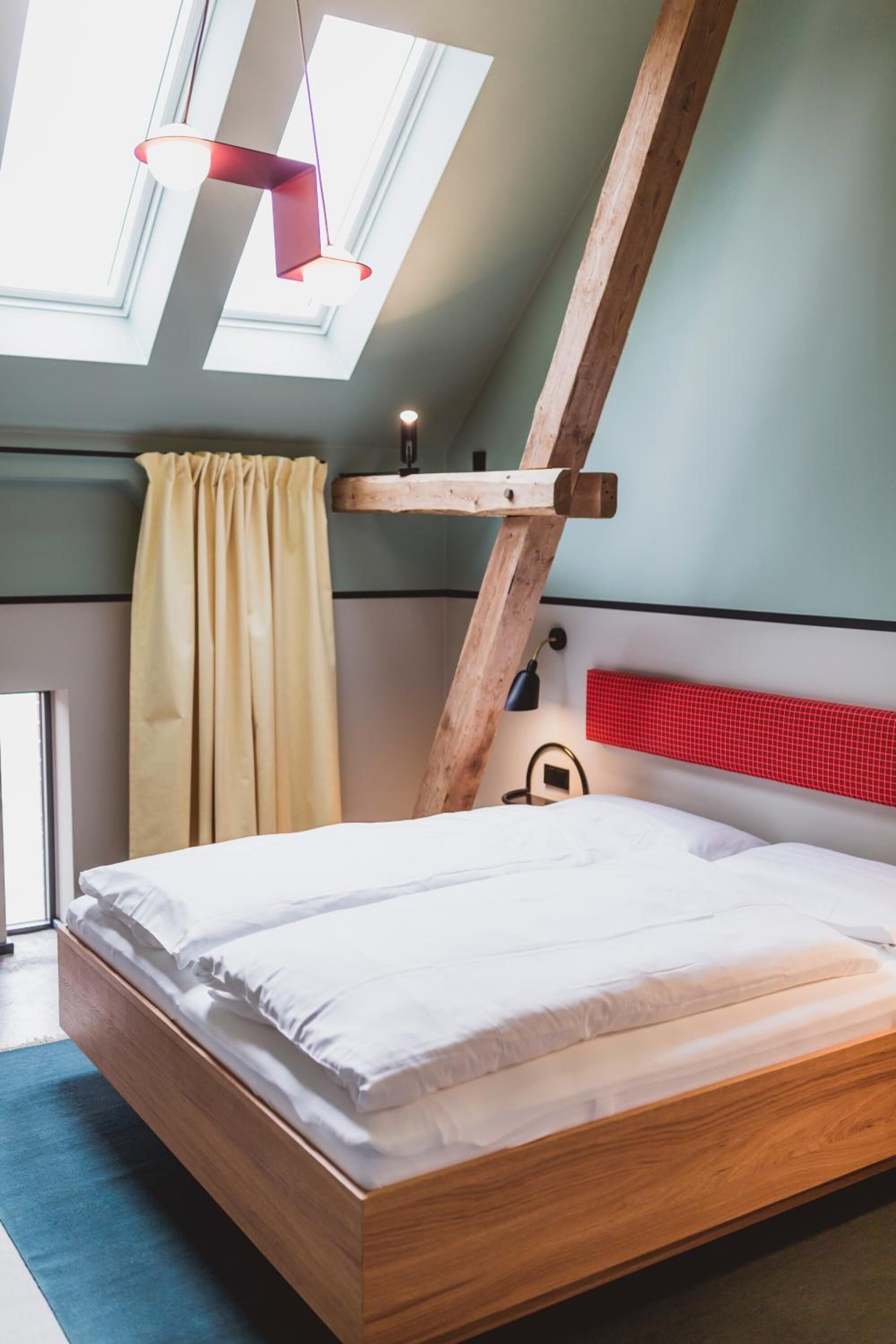 Une chambre avec un plafond en pente, un puits de lumière, un cadre de lit en bois et une tête de lit rouge.