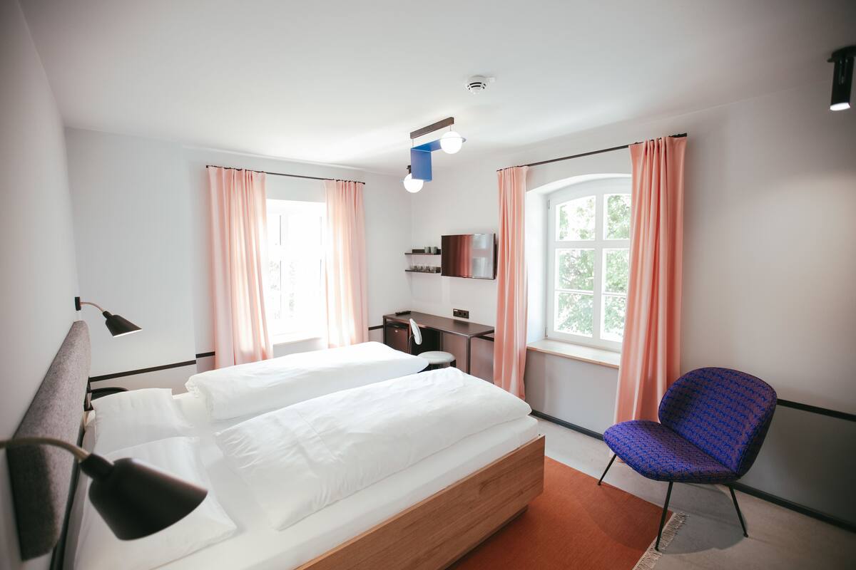 A modern hotel room with two beds, a desk, a chair, and a window with curtains.