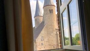 A room with a bed and a window overlooking a castle with three towers.