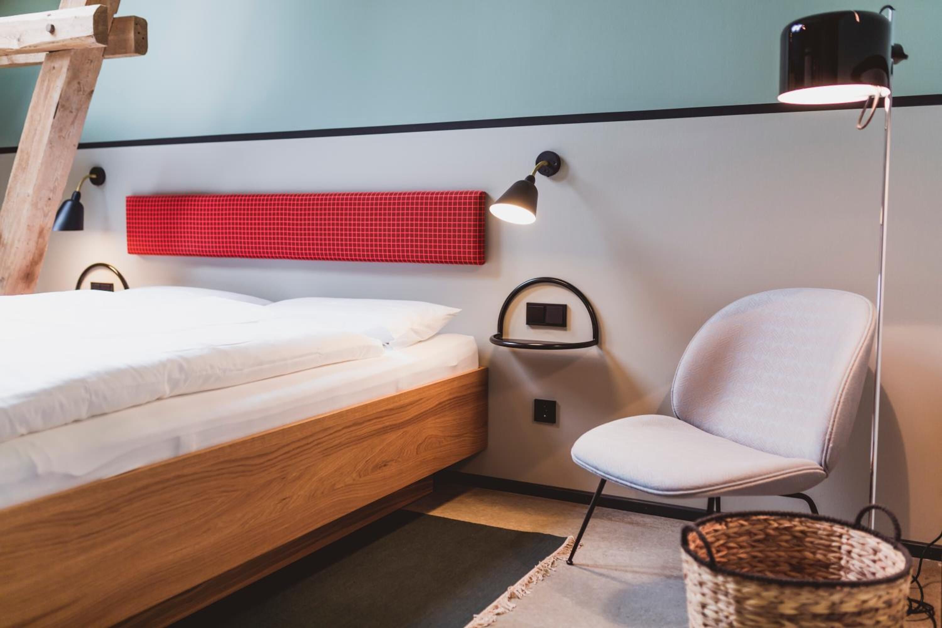 Ein Schlafzimmer mit einem hölzernen Bett, einem roten karierten Kopfteil, einem weißen Stuhl und einer Stehlampe.