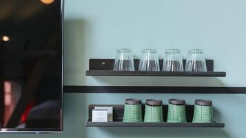 A wall-mounted shelf with four clear glass bottles and four green ceramic containers with lids.