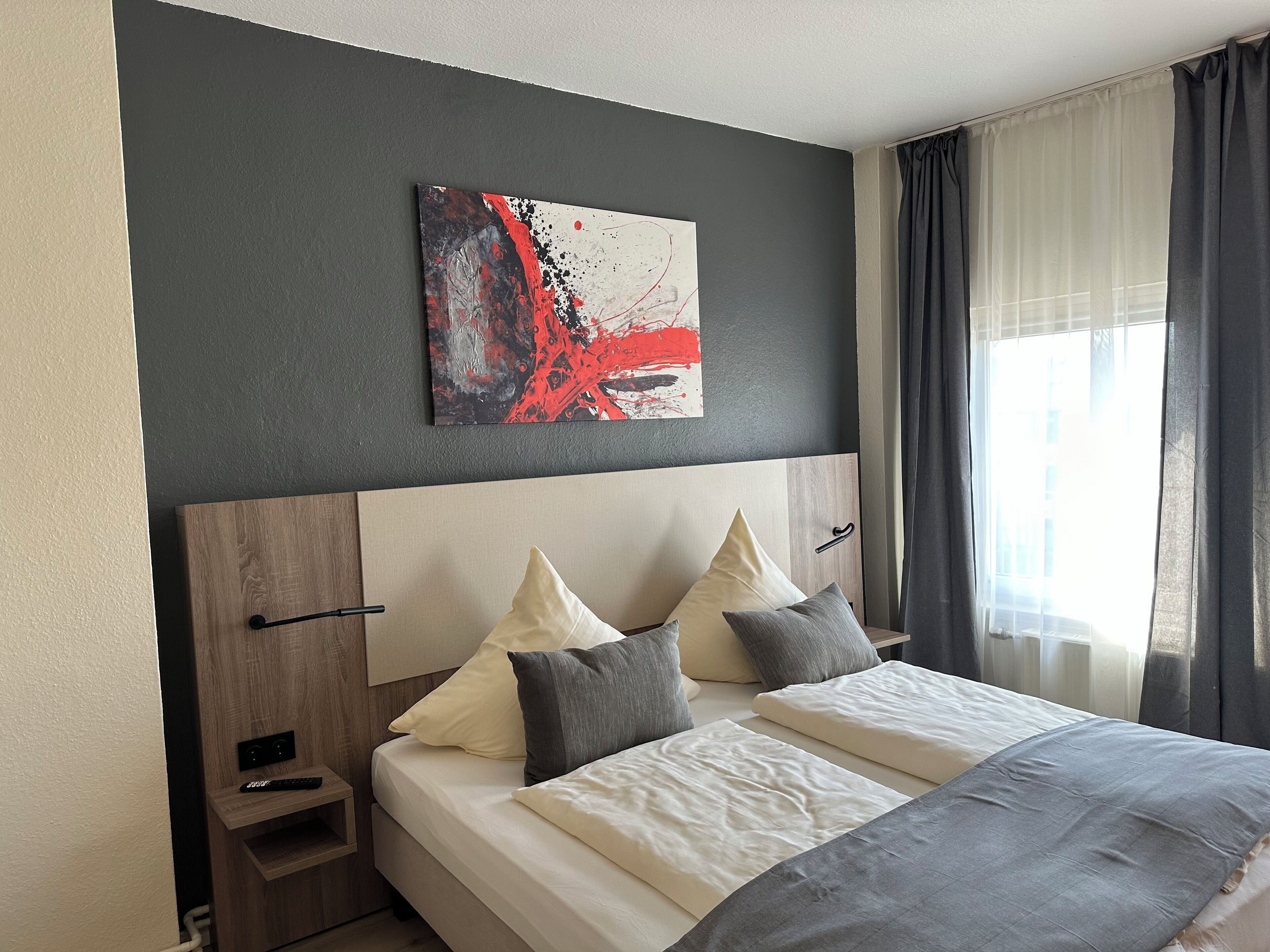 Une chambre à coucher moderne avec un grand lit, une tête de lit dotée de rangements, une table de chevet et un tableau au mur.