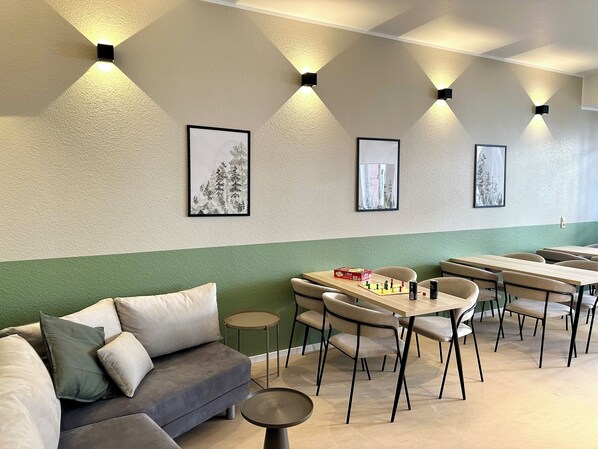Un espacio lounge moderno con sofá, mesas y sillas, que presenta obras de arte e iluminación ambiental.