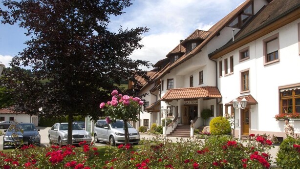 A traditional building with a white facade and a tiled roof, a visible entrance with steps, and parked cars in the foreground. - Hotel-Restaurant Hirsch Berghaupten (Berghaupten)