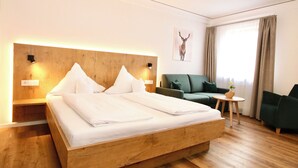 A hotel room with a large bed, a green sofa, a small table with a vase, and a deer artwork on the wall. - Hotel-Restaurant Hirsch Berghaupten (Berghaupten)