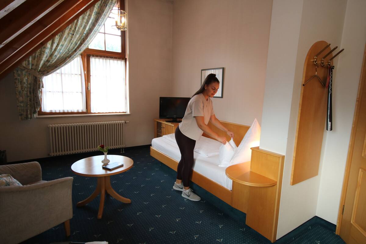 A hotel room with a bed, a small round table with a vase, a TV, and a coat rack.